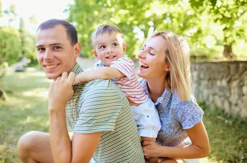 Mom and dad are playing with their toddler son outside at the park.