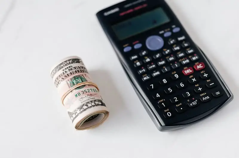 Some rolled up cash and a calculator next to it. Representing that you should choose a strategy that works for you, to invest and work towards becoming a millionaire.