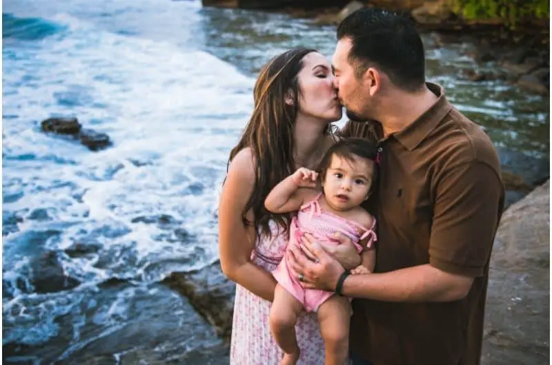 A happily married couple kissing and holding their baby girl. They're happy to be secured and confident in their financial future.