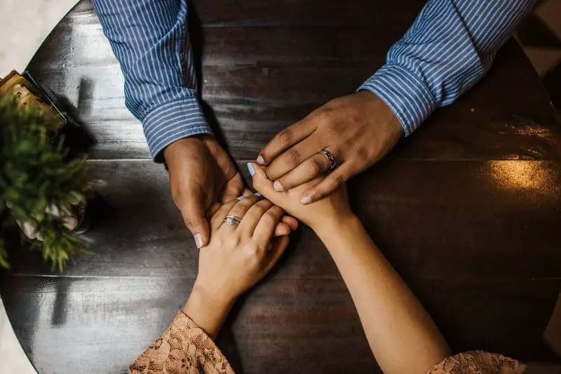 A young couple are holding hands, trying to work out financial issues that they are having, mostly because of him.