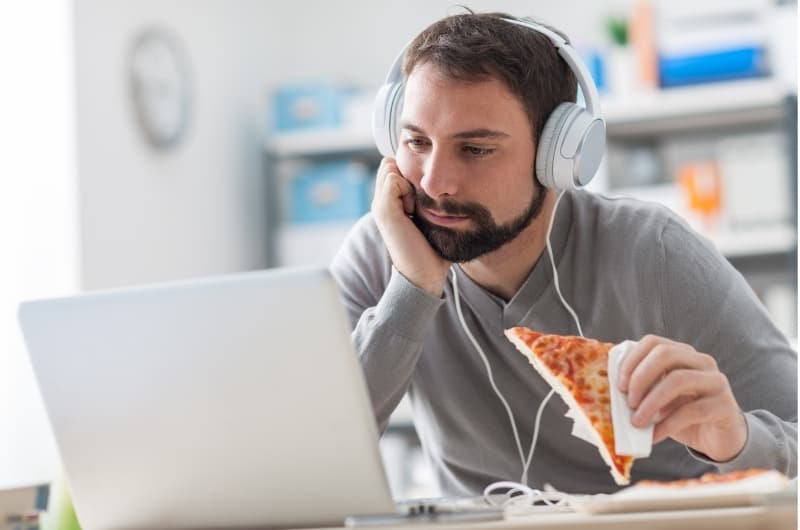 A lazy boyfriend, who is currently unemployed, is sitting in front of his computer and eating pizza, not doing anything to get a job.