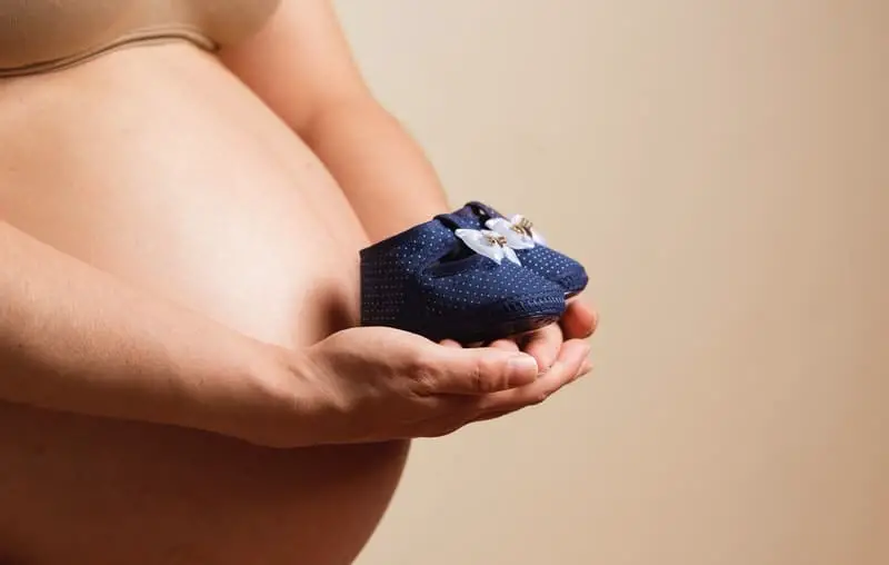 A pregnant woman is holding out her future newborns baby shoes.