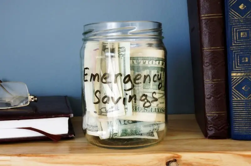 An emergency fund jar on a shelf, with lots of individual US bills inside.