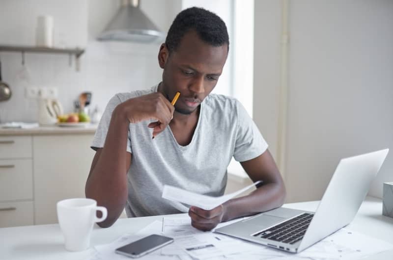 A young man is sitting at his desk reviewing the expensive bill he just received from his financial advisor. He isn't too happy about it.