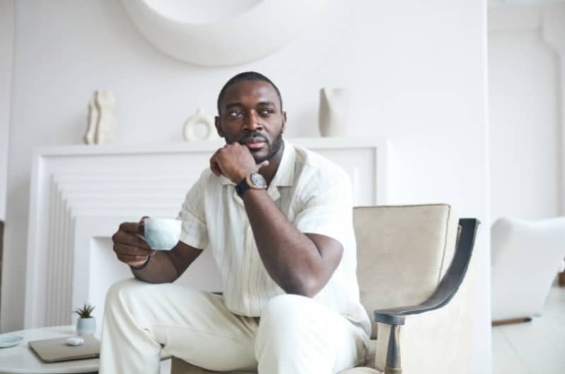 A wealthy self-made entrepreneur is sitting in his luxury home, drinking coffee and thinking of his next business idea.