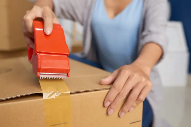 Young girl is moving out from her current place and is taping a box of stuff to move.