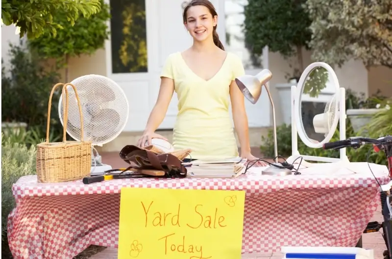 A young girl is standing behind a table with yard sale items.