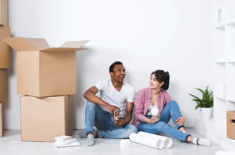 A young girl is moving in with her boyfriend, they're drinking coffee on the floor as they take a break from unpacking.