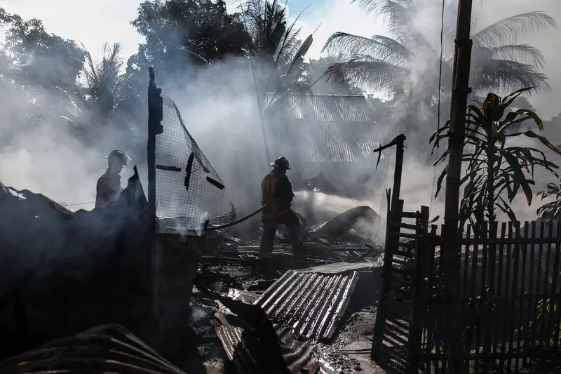 Firemen are hosing down a house that has collapsed after being on fire for some time.