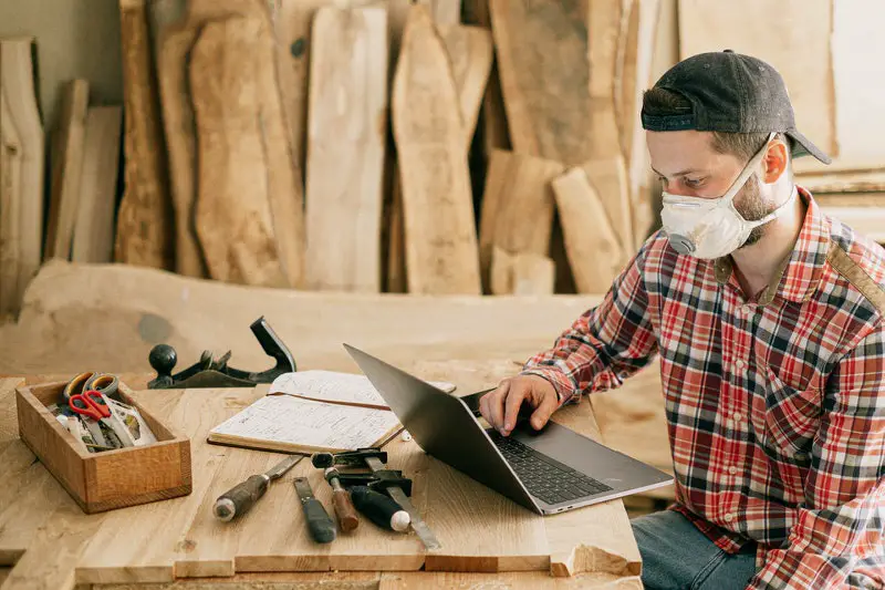 A young man who is refurbishing furniture is on his laptop looking at instructions for his latest project.