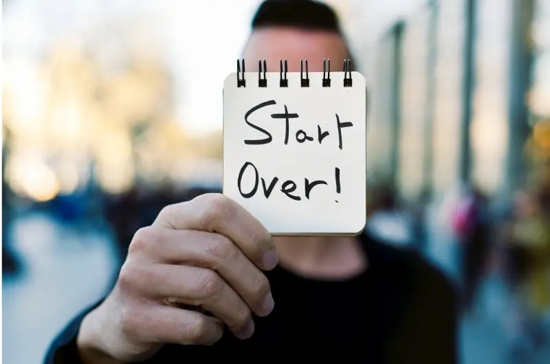 A young man is outside and is holding out a message on a pad that says, "start over."