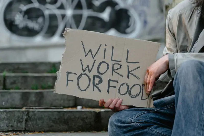A young man is holding a "will work for food" cardboard sign to get food money while he's homeless.