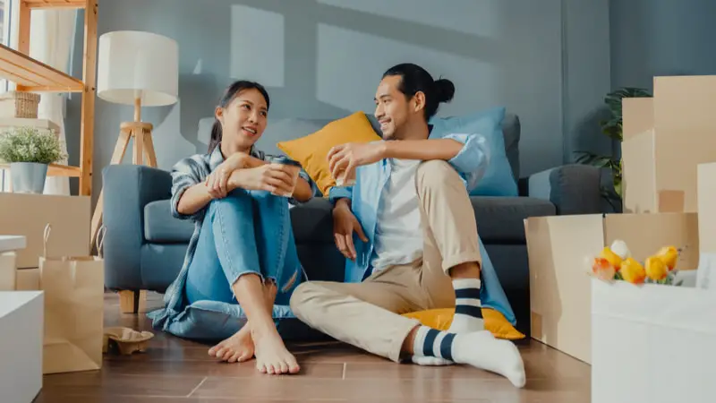 A young couple is sitting on the floor in a new apartment that they've just rented.