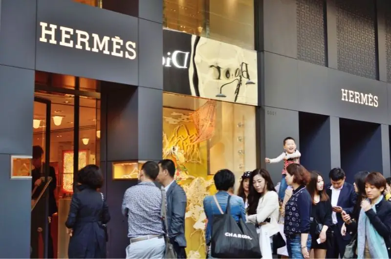 A crowd of people are waiting outside of Hermes to buy handbags as an investment