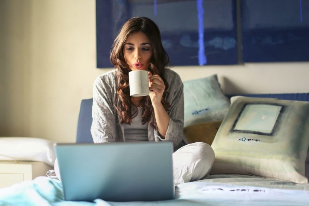 A young woman is sitting on her bed working from home