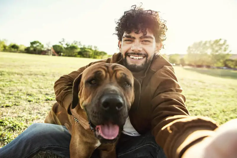 A young man is taking a picture with a dog that he's walking for his client.