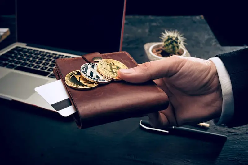 A man holding his wallet with various physical cryptocurrency coins on top.