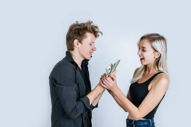 A young couple are smiling as they both hold several hundred dollar bills in their hands.
