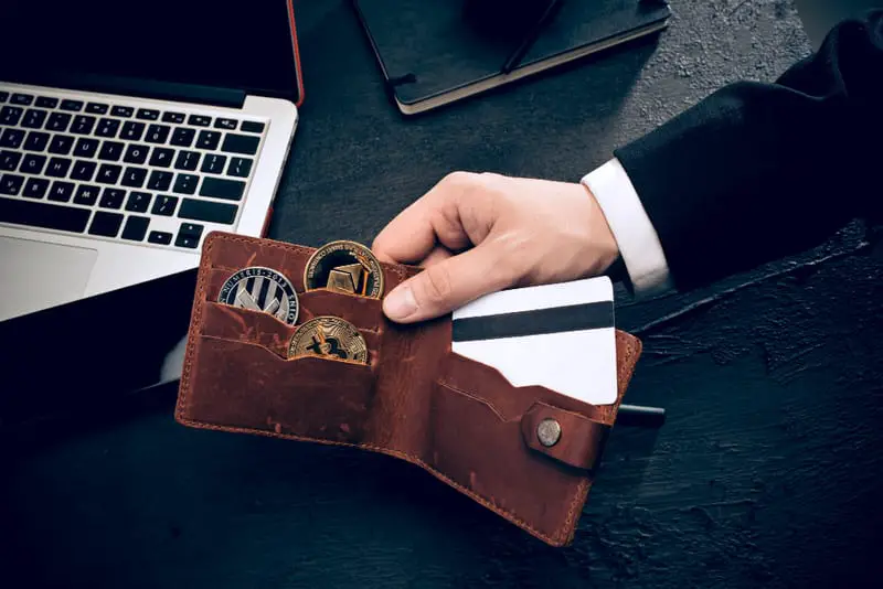 A man holding a wallet with different cryptocurrencies, such as litecoin, etherium, and bitcoin.