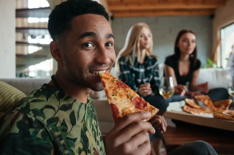 A young man eating pizza with his friends. Food is one of the major life expenses.