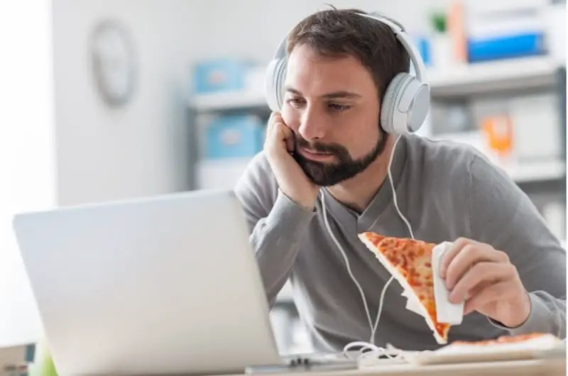 A lazy boyfriend, who is currently unemployed, is sitting in front of his computer and eating pizza, not doing anything to get a job.