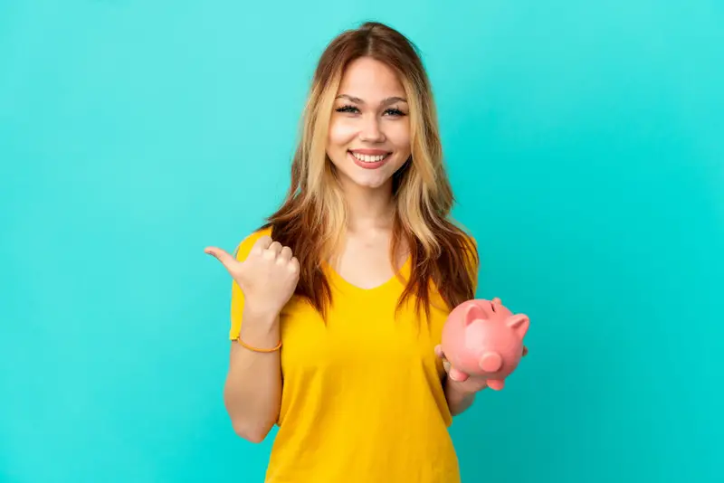 A young woman is holding a piggy bank and smiling.