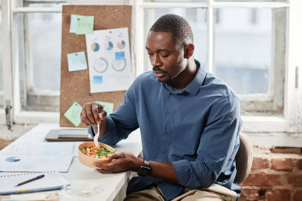 A young man is having his homemade lunch at his work desk to save money