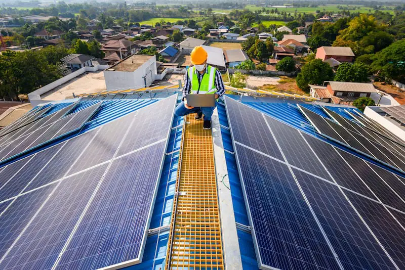 An electrical engineer is on the roof of a house examining the installed solar panels